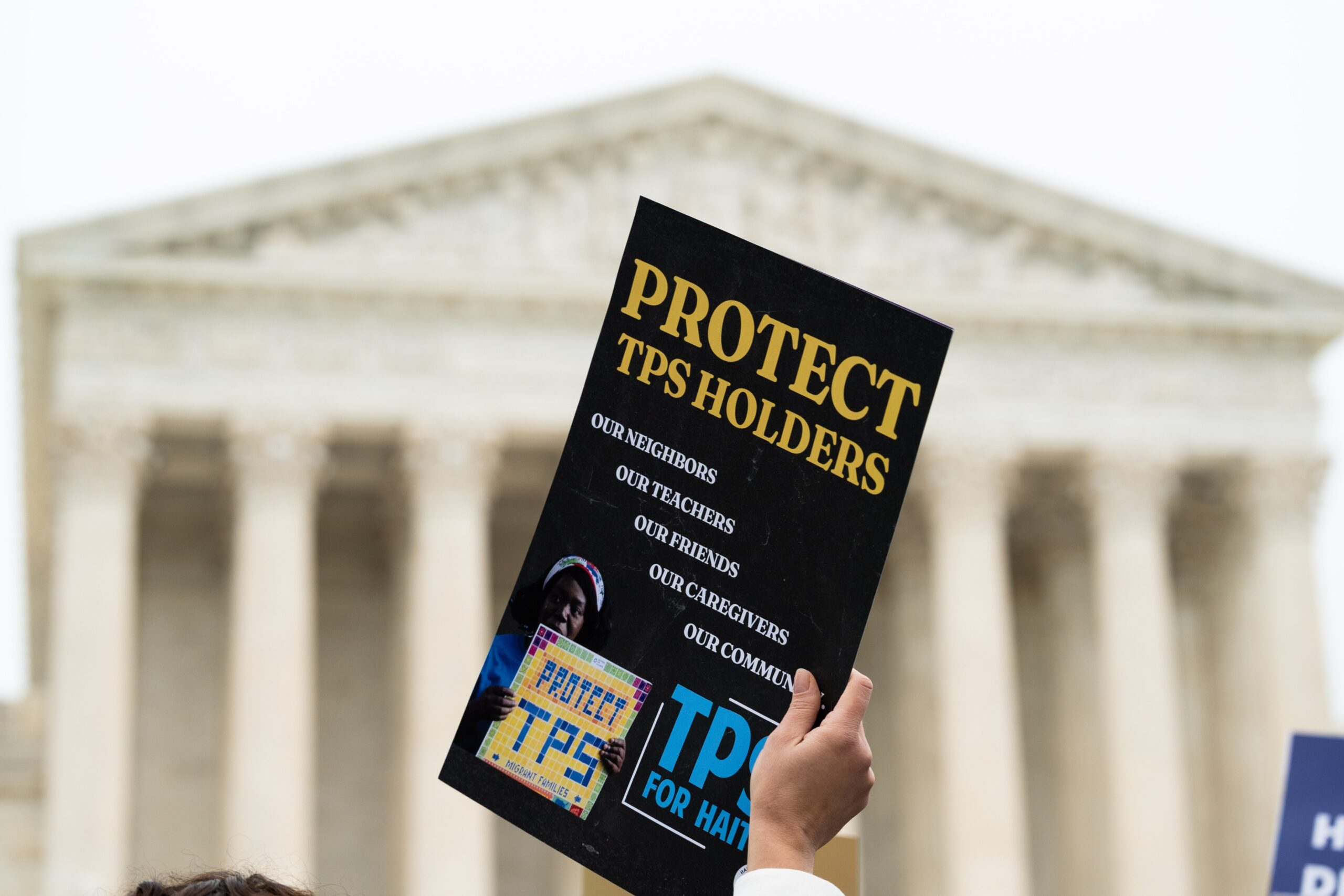 Hand holding a sign that says "Protect TPS holders" in front of the U.S. Supreme Court