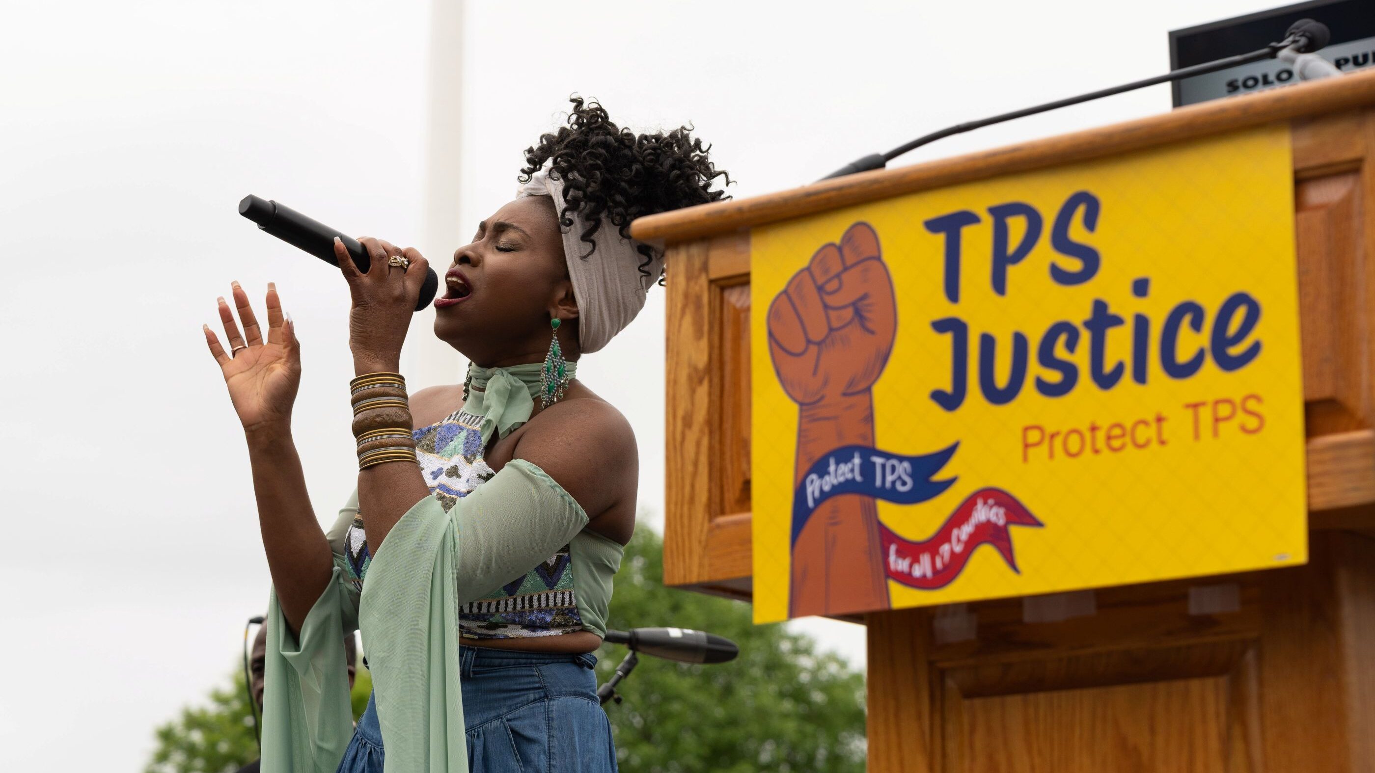 Singer in front of podium with sign saying :TPS Justice