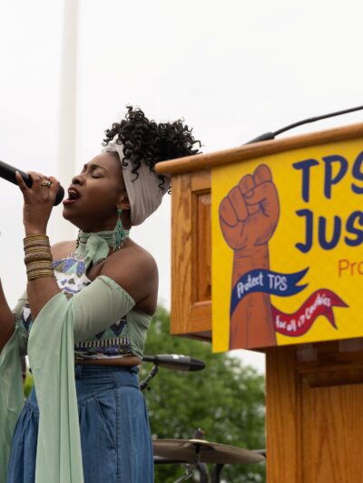 Singer in front of podium with sign saying :TPS Justice