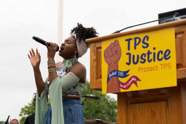 Singer in front of podium with sign saying :TPS Justice