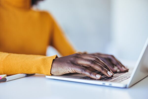 Photo of woman wearing yellow sweater typing on a laptop placed on a desk.